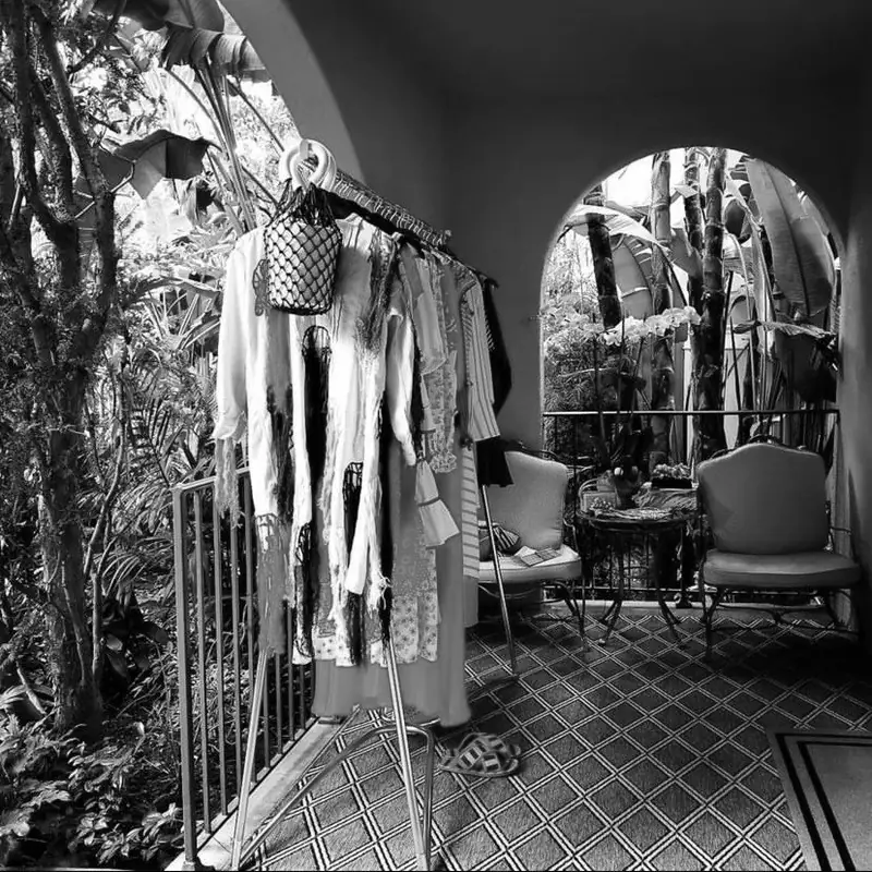 Resort wardrobe styling — white kaftans and holiday pieces on a rail beside a tropical garden