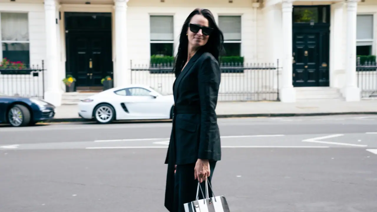 Woman in a black tailored suit carrying a shopping bag on a white stucco London street